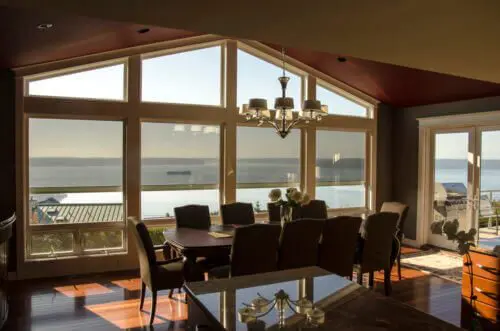Dining area with large windows overlooking a serene lake at sunset.