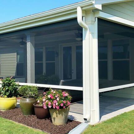 House porch enclosed with mesh screens and decorated with potted plants.